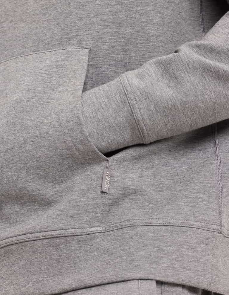 A person in a gray Men's StretchTech Hoodie by Cozy Earth has their hand in the front pocket, highlighting the fabric's texture and details. |Color:Coal Heather