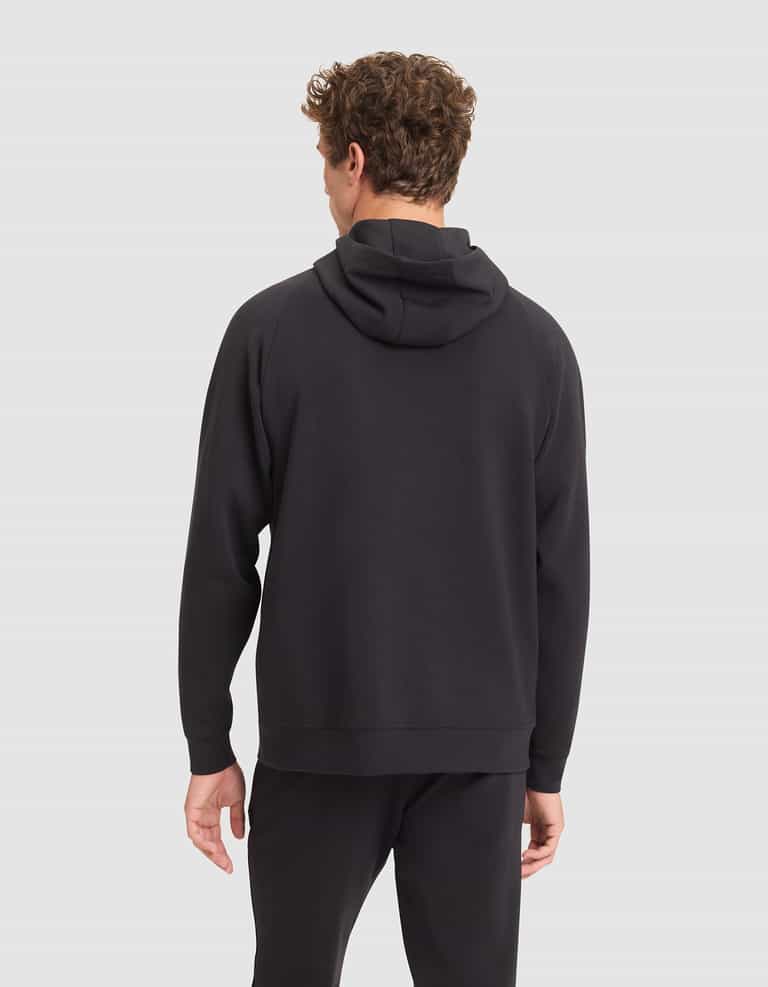 A man with curly hair faces away from the camera, wearing a Cozy Earth Men's StretchTech Hoodie in black and black pants against a light gray background. |Color:Jet Black