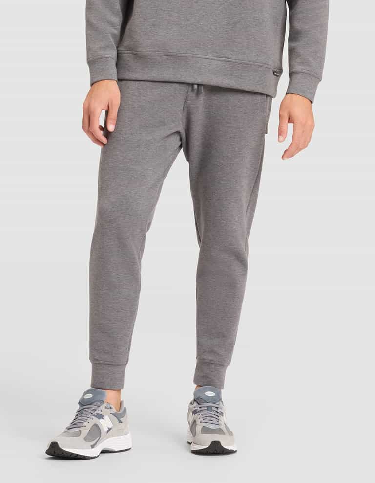 A person is shown from the waist down, wearing Cozy Earth's Men's StretchTech Jogger in gray with a matching sweatshirt and gray-white sneakers, standing against a plain white background. |Color:Coal Heather