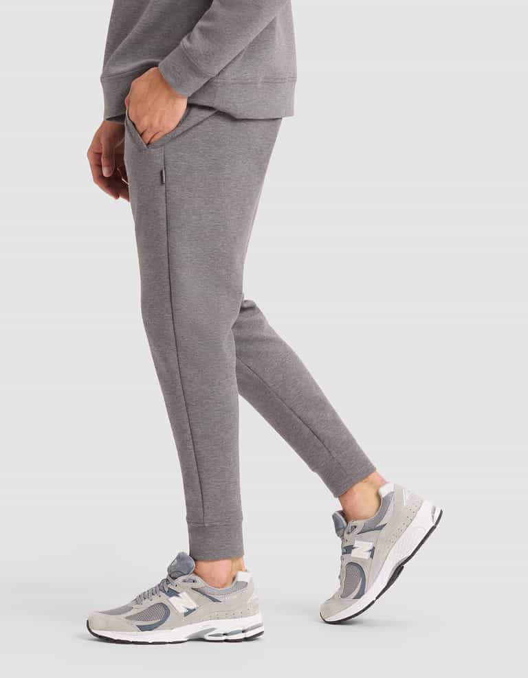 A person is shown from the shoulders down, wearing Cozy Earth's Men's StretchTech Jogger in grey with grey-and-white sneakers, standing on a white background with one hand in their pocket. |Color:Coal Heather