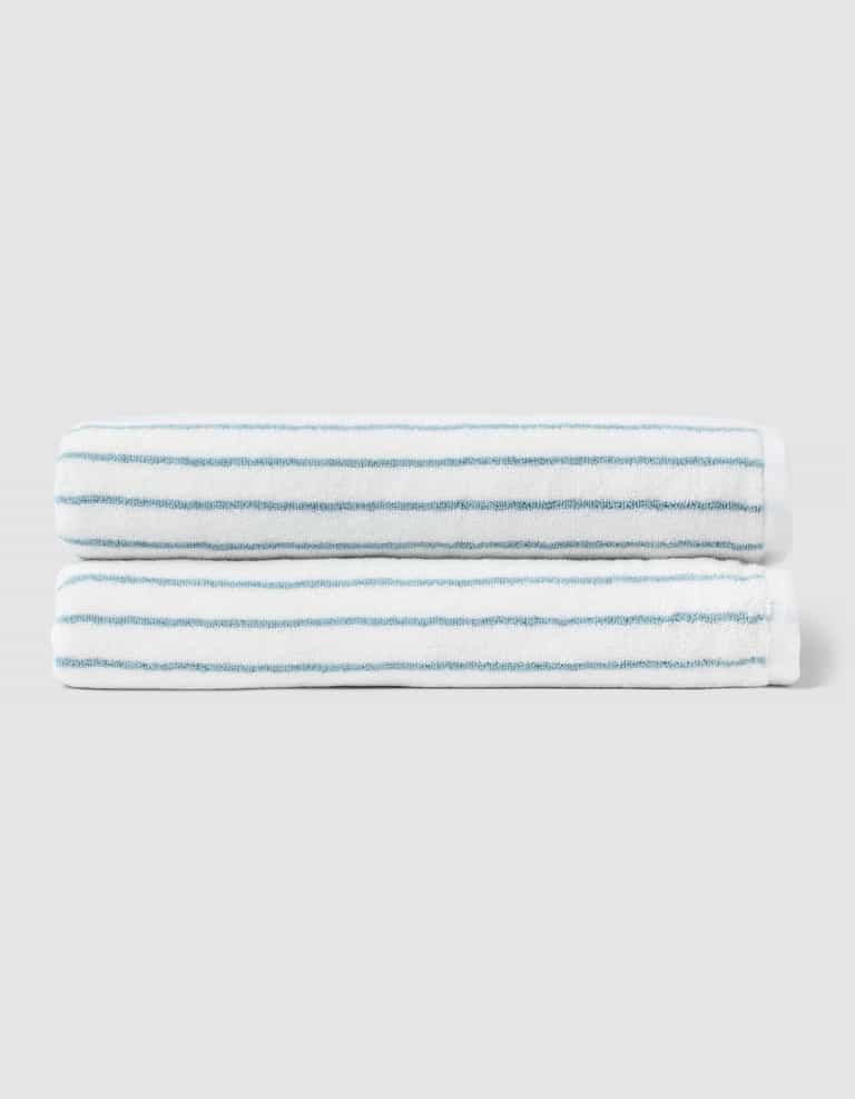 Two neatly folded Cozy Earth Striped Luxe Bath Sheets, featuring thin light blue stripes, are stacked together against a plain light gray background. |Color:Brook Stripe