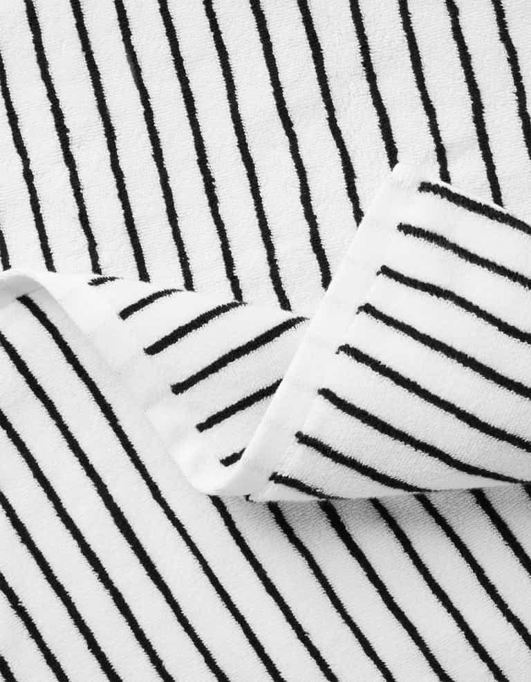 A close-up of Cozy Earth’s Striped Luxe Bath Towels shows white textured fabric with evenly spaced black vertical stripes, partially folded at the center. |Color:Black Stripe