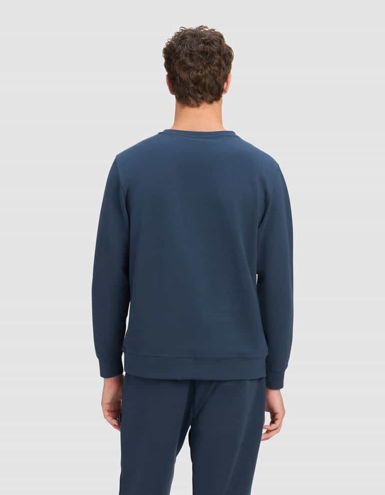 A person with short curly brown hair faces away from the camera, wearing the Cozy Earth Men's StretchTech Crewneck in dark blue against a plain light gray background.|Color:Eclipse
