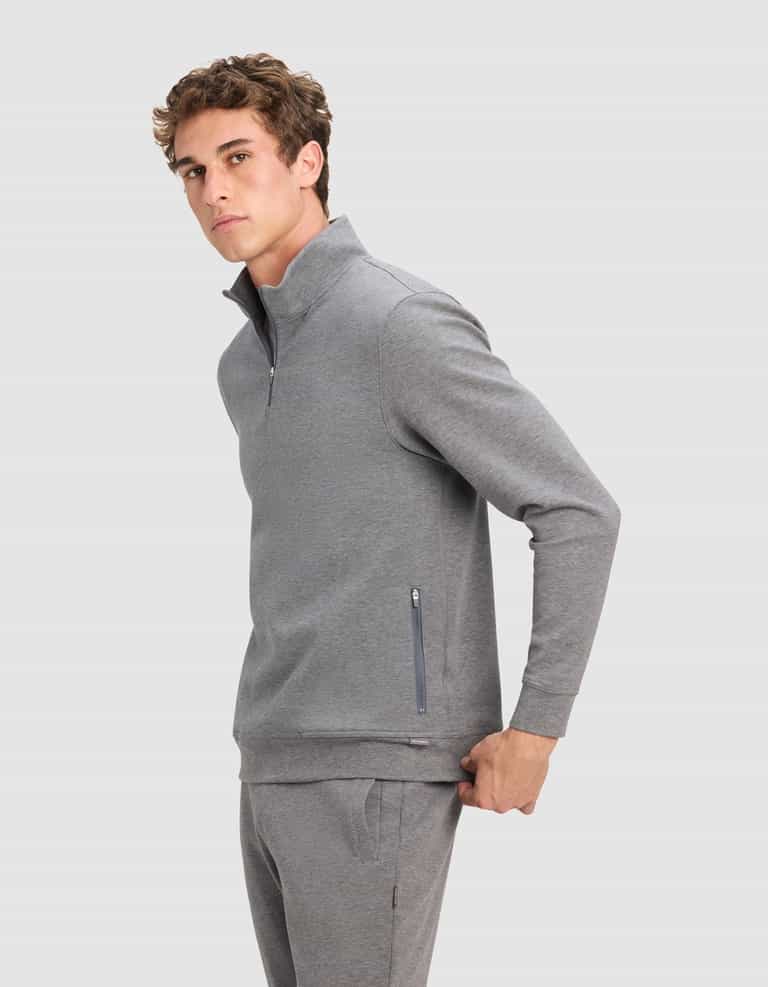 A young man wears the Cozy Earth Men's StretchTech Quarter Zip in light gray with matching sweatpants, standing against a plain background and looking at the camera with a neutral expression.|Color:Coal Heather
