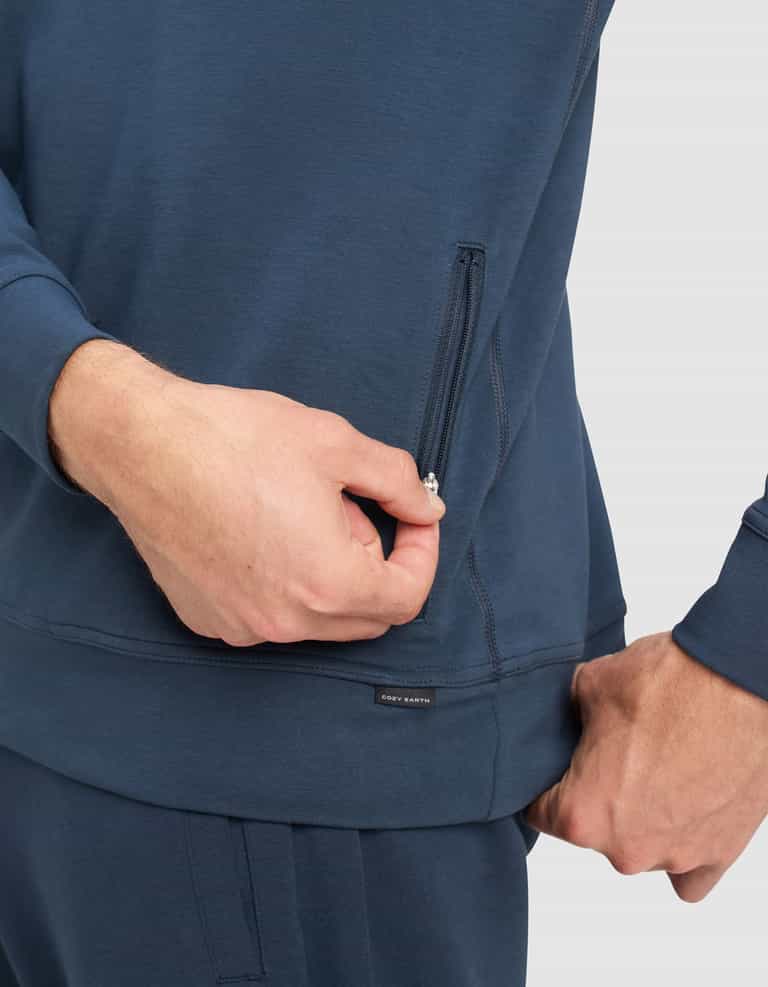 A man wearing Cozy Earth Men's StretchTech Quarter Zip and matching pants is pulling the zipper of a side pocket on the top, set against a plain light gray background.|Color:Eclipse