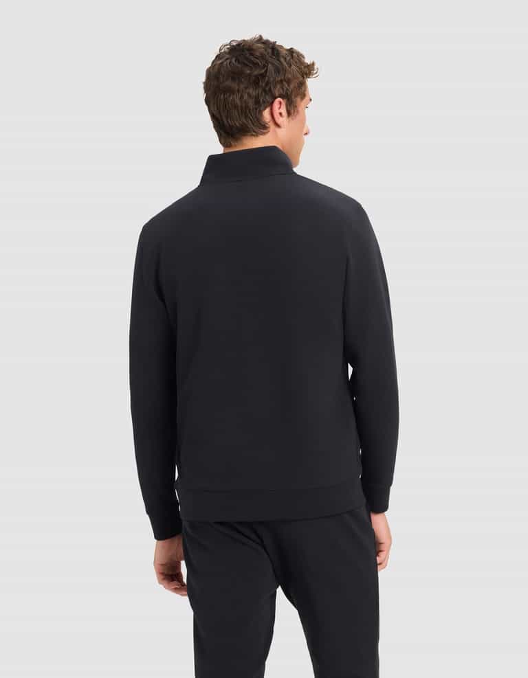 A man with short, curly brown hair is shown from behind, wearing Cozy Earth's Men's StretchTech Quarter Zip in black, paired with matching black pants and standing against a plain light gray background.|Color:Jet Black