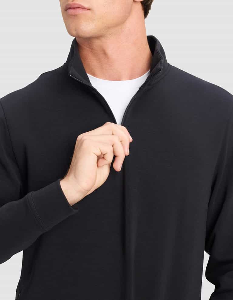 A person is shown unzipping the collar of a Cozy Earth Men's StretchTech Quarter Zip, worn over a white shirt, with their face partially visible against a plain light gray background.|Color:Jet Black