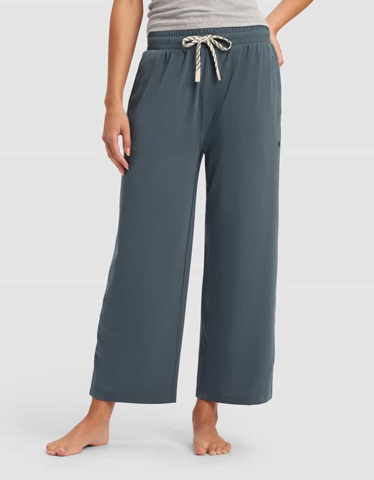 A person stands barefoot wearing Cozy Earth’s Women's Studio Cropped Wide Leg Pant in blue-gray with an elastic waistband and striped drawstring, paired with a gray top; their left hand rests on their hip.|Color:Dawn