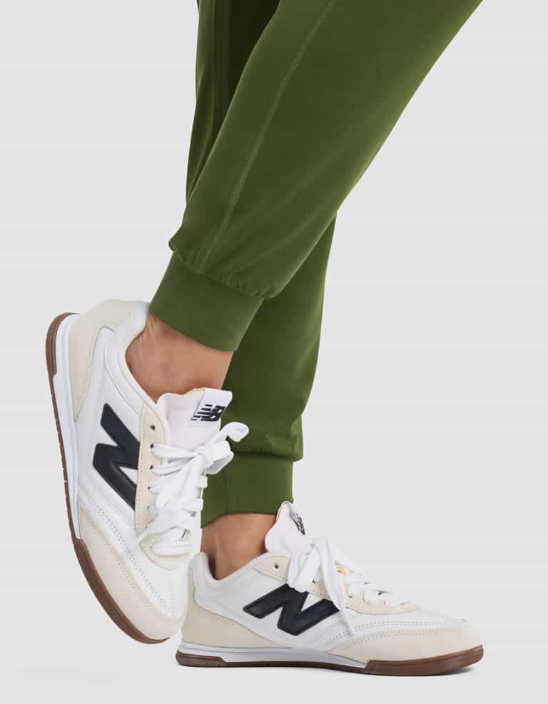 A person wearing Cozy Earth Women's Studio Jogger in green and white New Balance sneakers with black "N" logos stands on tiptoes against a plain light background.|Color:Grove