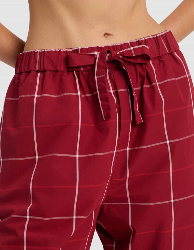 A close-up of the Cozy Earth Women's Sutton Long Sleeve Pajama Set shows red plaid pants with a white grid pattern and fabric waist tie, pictured from waist to mid-thigh.|Color:Garnet Windowpane