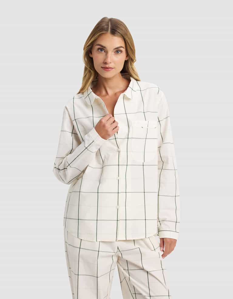 A woman with light brown hair models the Cozy Earth Women's Sutton Long Sleeve Pajama Set in cream with a green windowpane check pattern, standing against a plain light gray background.|Color:Bone Windowpane