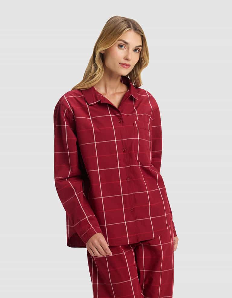 A woman poses against a light gray background wearing the Cozy Earth Women's Sutton Long Sleeve Pajama Set in red plaid with a white windowpane pattern, featuring a button-up top and matching pants.|Color:Garnet Windowpane