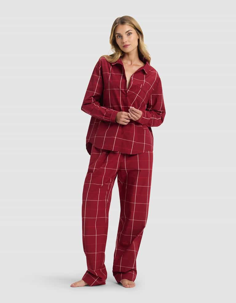 A woman stands barefoot against a light gray background wearing the Cozy Earth Women's Sutton Long Sleeve Pajama Set—featuring a matching button-up top and loose-fitting pants in red plaid.|Color:Garnet Windowpane