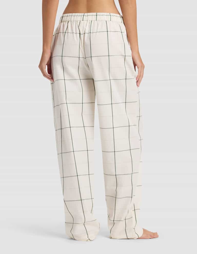 A person is barefoot, shown from the waist down, wearing Cozy Earth Women's Sutton Long Sleeve Pajama Set pants in a green windowpane check with an elastic waistband. The background is plain light gray.|Color:Bone Windowpane
