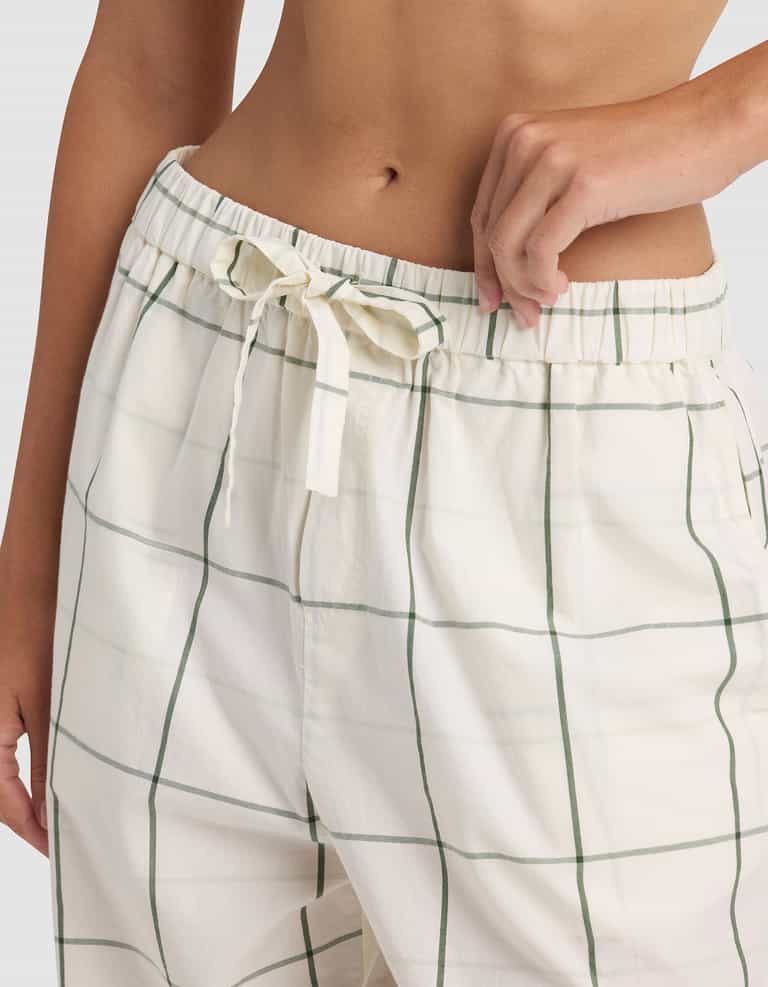A person is shown from waist to mid-thigh wearing Cozy Earth's Women's Sutton Long Sleeve Pajama Set pants—cream-colored, high-waisted with green plaid lines and a fabric bow at the elastic waistband.|Color:Bone Windowpane