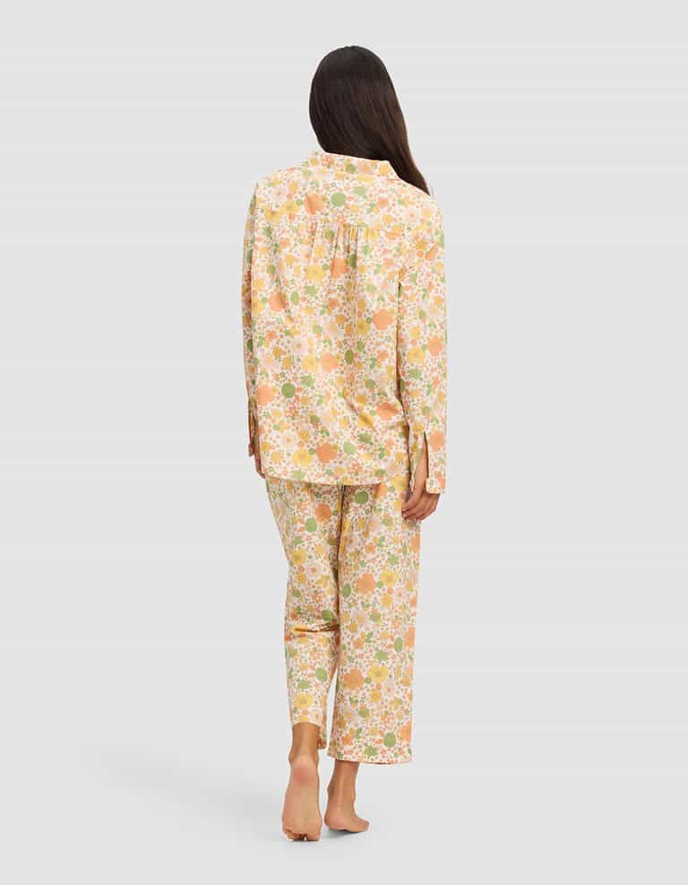 A woman stands barefoot, facing away, wearing the Cozy Earth Women's Sutton Long Sleeve Pajama Set in a pastel floral print with long sleeves and full-length pants, set against a plain light background.|Color:Wildflower