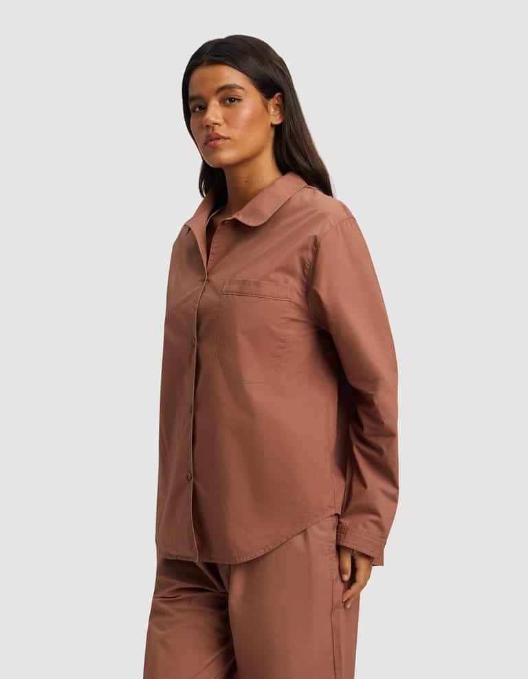 A woman with long dark hair confidently wears the Cozy Earth Women's Sutton Long Sleeve Pajama Top in dusty rose, paired with matching pants, standing against a plain light gray background.|Color:Saddle