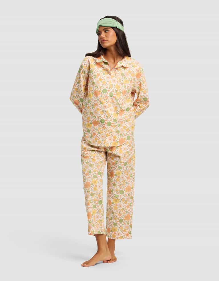 A woman stands barefoot on a plain background, hands behind her back and looking to the side, wearing the Cozy Earth Women's Sutton Long Sleeve Pajama Top and a light green sleep mask.|Color:Wildflower