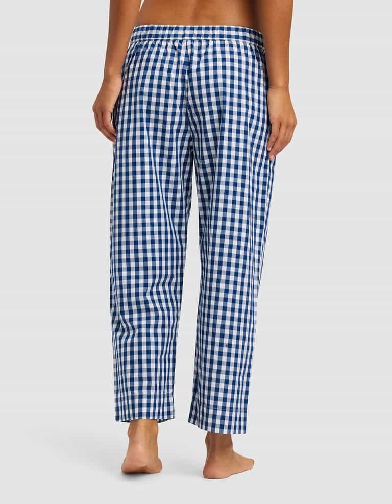 A woman stands barefoot, facing away, wearing Cozy Earth Women's Sutton Cropped Pajama Pant in blue and white gingham with an elastic waistband, set against a plain light background.|Color:Pacific Gingham