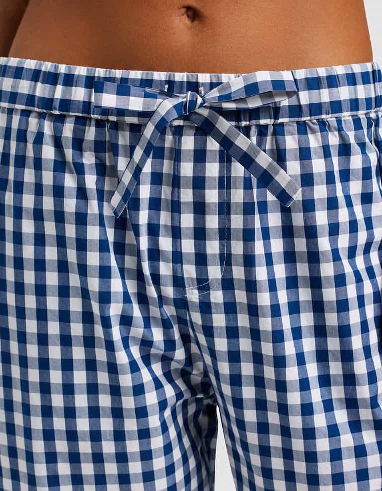 Close-up of a person wearing Cozy Earth Women's Sutton Cropped Pajama Pant, featuring a blue and white gingham pattern and a drawstring bow at the waistband.|Color:Pacific Gingham