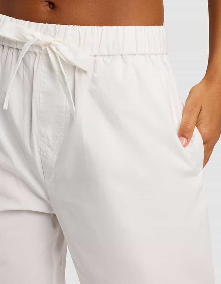 Close-up of a person wearing Cozy Earth's Women's Sutton Cropped Pajama Pant in white, with their right hand in the pocket. The background is plain light gray.|Color:White