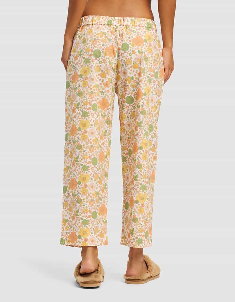 A person stands barefoot with their back to the camera, wearing Cozy Earth's Women's Sutton Cropped Pajama Pant in a loose floral print, paired with fuzzy beige slippers, against a plain background.|Color:Wildflower