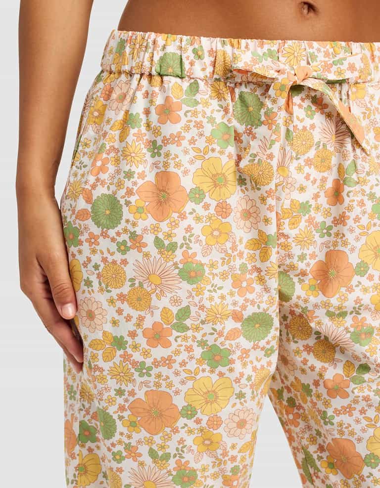 A close-up of a person wearing Cozy Earth's Women's Sutton Cropped Pajama Pant, featuring a vibrant floral print in orange, yellow, and green. One hand is in the pocket, highlighting the waist and upper leg area.|Color:Wildflower