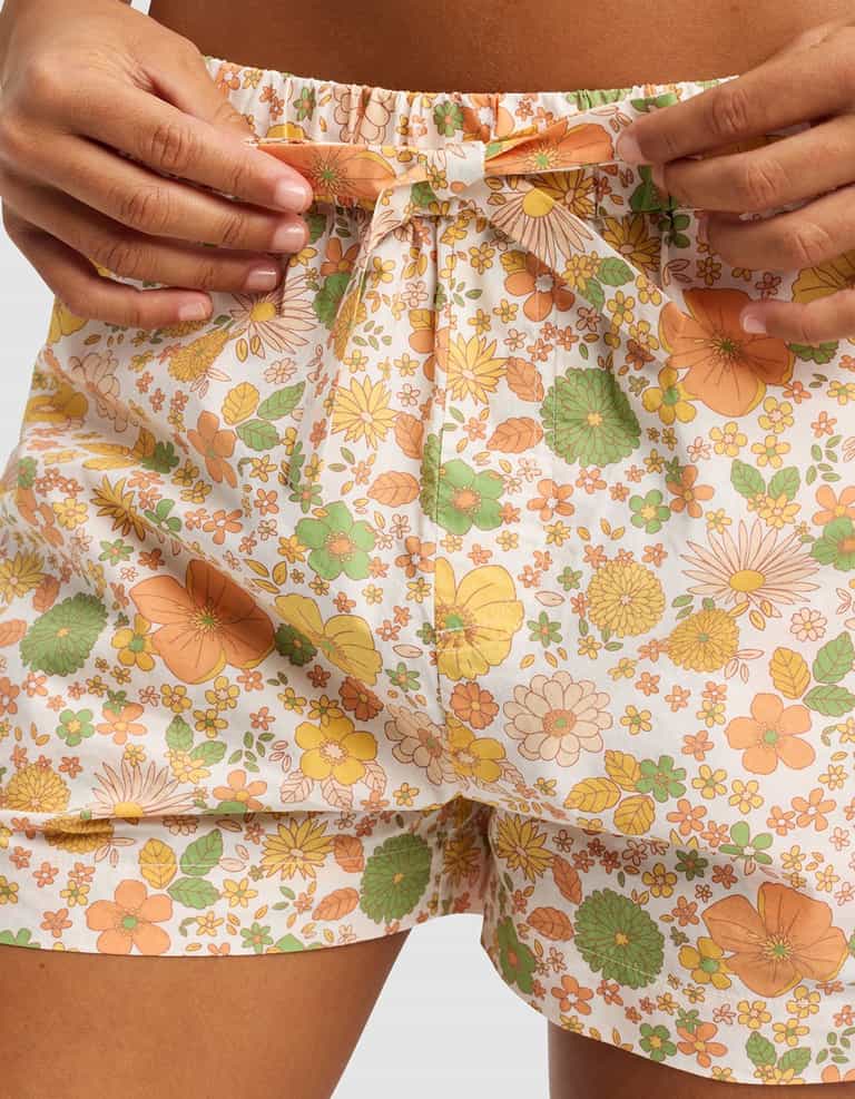Close-up of a person’s hands adjusting the drawstring on Cozy Earth Women's Sutton Pajama Short, featuring a high-waisted fit and a vibrant floral pattern in orange, yellow, and green on a white background.|Color:Wildflower