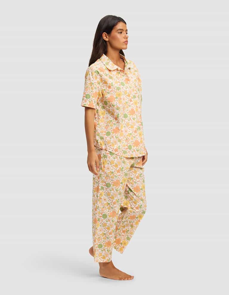 A woman stands barefoot in the Cozy Earth Women's Sutton Short Sleeve & Pant Pajama Set—loose-fitting, pastel floral print pajamas—against a plain light gray background.|Color:Wildflower