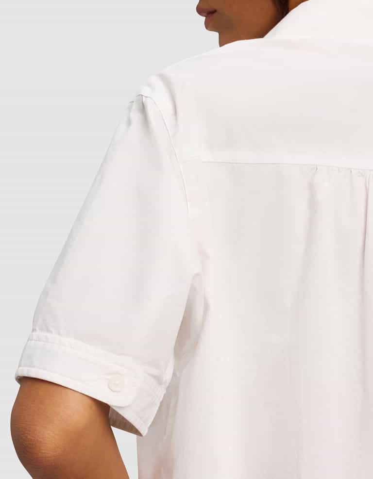 Close-up of a woman wearing the Cozy Earth Women's Sutton Short Sleeve Pajama Top, shown from the back and side. Focus on the sleeve, cuff button, and back shoulder detail. Background is plain light gray.|Color:White