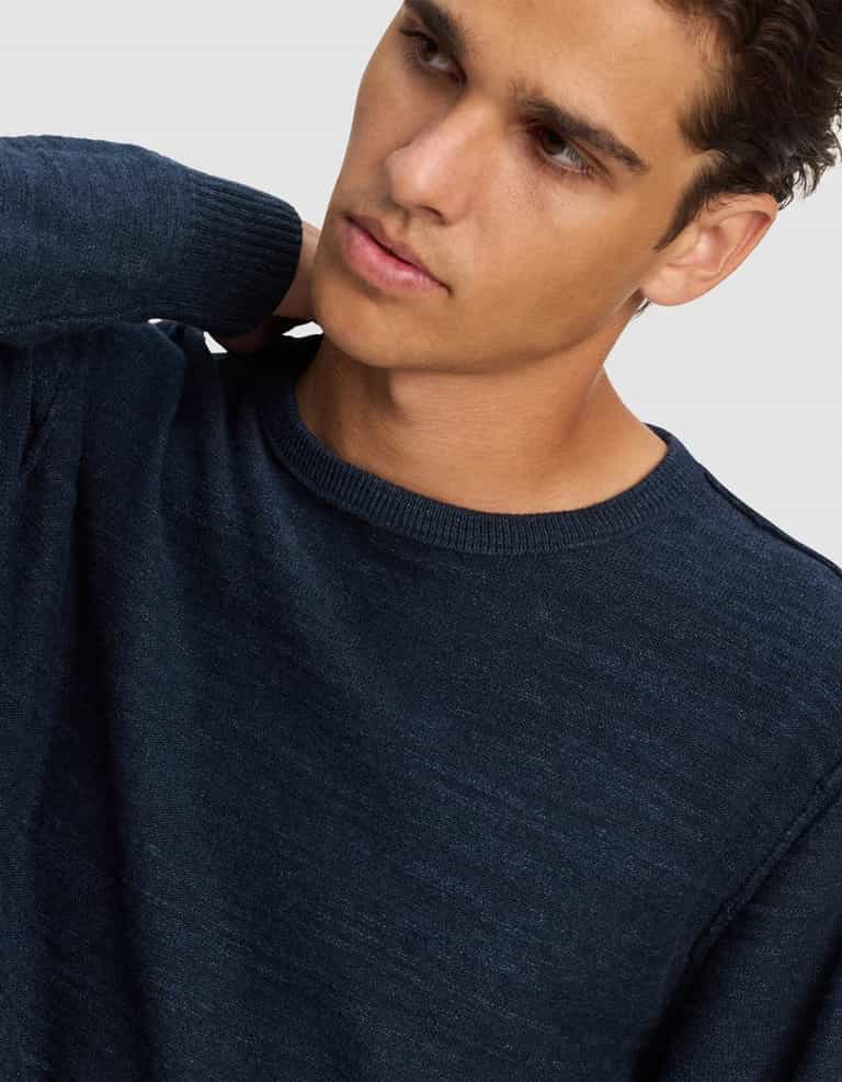 A young man with short brown hair, wearing the Cozy Earth Men's Tate Crewneck, looks off to the side with his hand behind his neck against a plain light background.|Color:Eclipse