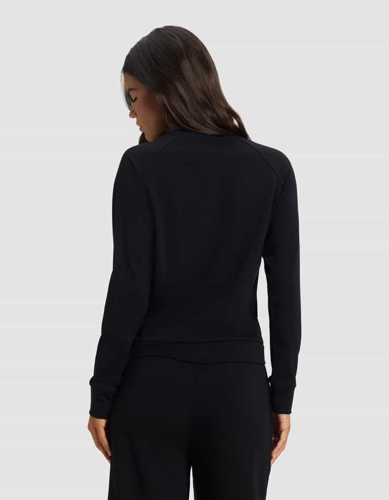 A woman with long dark hair faces away, wearing the Cozy Earth Women's Brushed Bamboo Pullover Crew in black, paired with matching black pants against a light gray background.|Color:Black