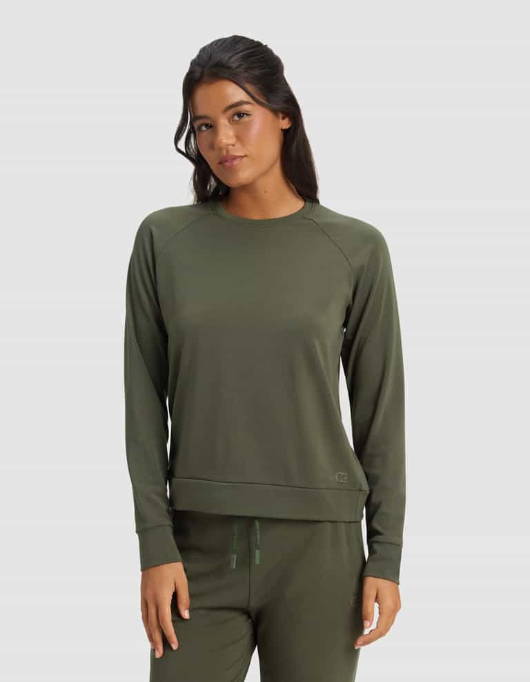A woman with long dark hair wears the Cozy Earth Women's Brushed Bamboo Pullover Crew in olive green, paired with matching pants, standing against a plain light gray background.|Color:Olive