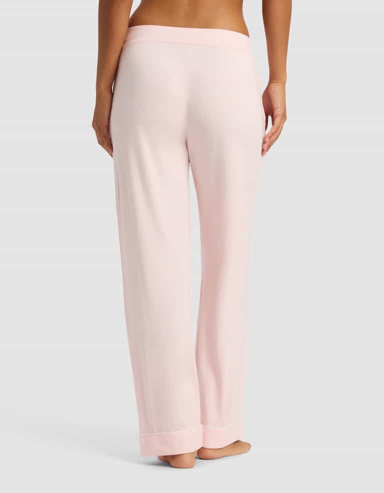 A woman is shown from the waist down wearing Cozy Earth Women's Bamboo Stretch-Knit Long Sleeve Pajama Set pants in light pink, standing barefoot against a plain gray background.|Color:Blossom