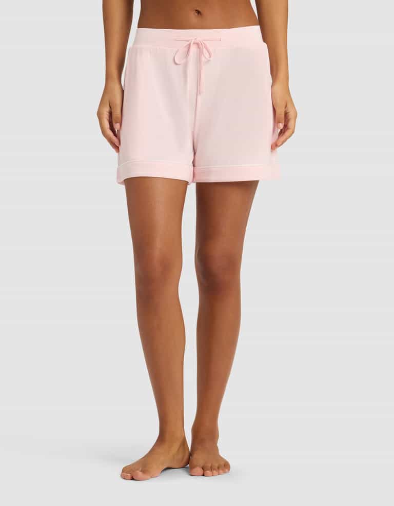 A person wearing Cozy Earth Women's Bamboo Stretch-Knit Pajama Shorts in pale pink stands barefoot on a light grey background; the image is cropped from the waist down.|Color:Blossom