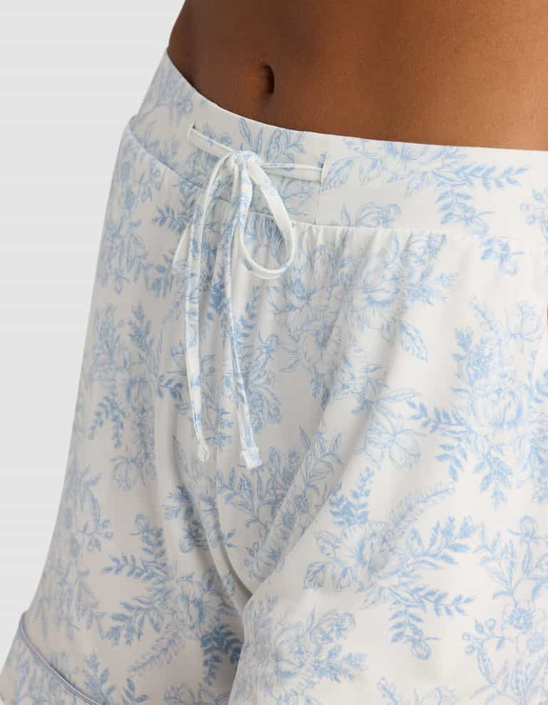 Close-up of a person wearing Cozy Earth Women's Bamboo Stretch-Knit Pajama Shorts, featuring a light blue floral pattern, drawstring waistband, and soft, comfortable fabric visible on the waist and upper thigh area.|Color:Sky Toile