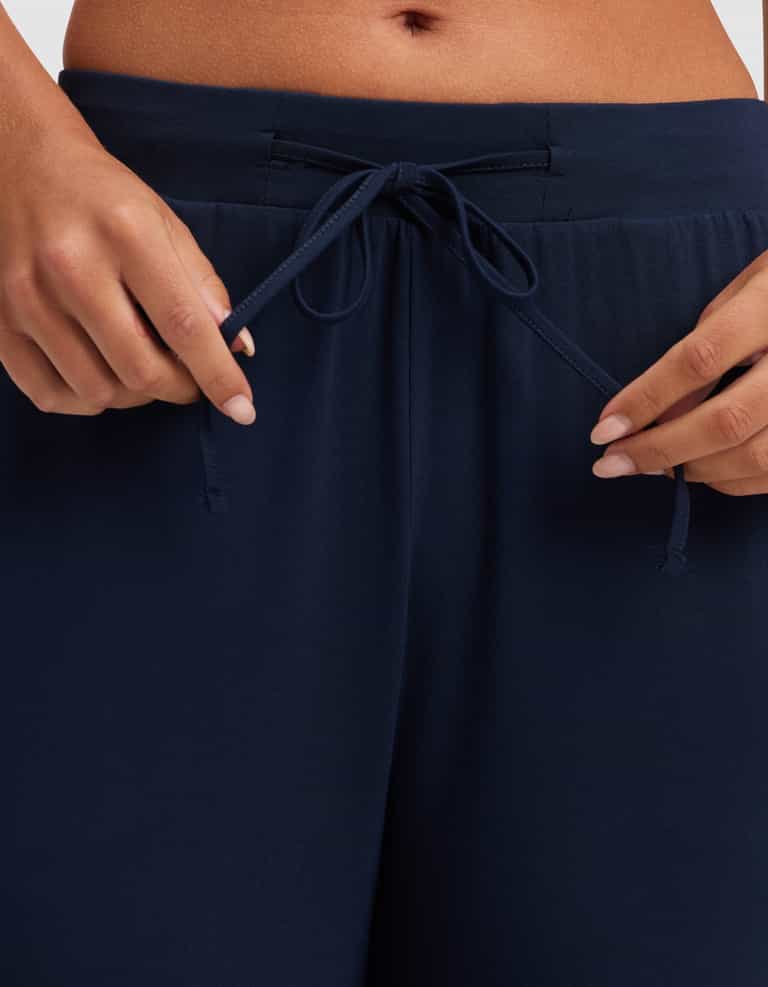 Close-up of hands adjusting the drawstring on HIDE Women's Bamboo Stretch-Knit Pajama Pant in navy blue, with a glimpse of midriff above the waistband. |Color:Navy