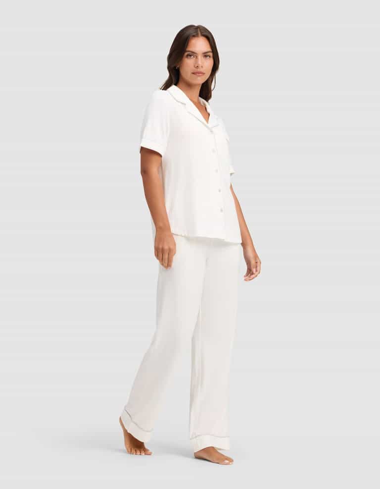 A woman stands barefoot against a plain background, wearing the Cozy Earth Women's Bamboo Stretch-Knit Short Sleeve & Pant Pajama Set. |Color:Ivory