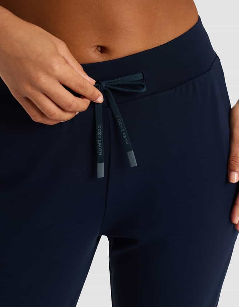 Close-up of a person adjusting the drawstring at the waistband of Cozy Earth Women's Brushed Bamboo Jogger Pant in dark navy blue, with "COZY EARTH" on the tips.|Color:Navy
