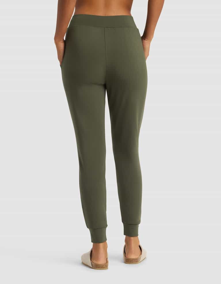 A person is seen from the back with hands in pockets, wearing Cozy Earth Women's Brushed Bamboo Jogger Pant in olive green and beige slip-on sandals against a plain white background.|Color:Olive