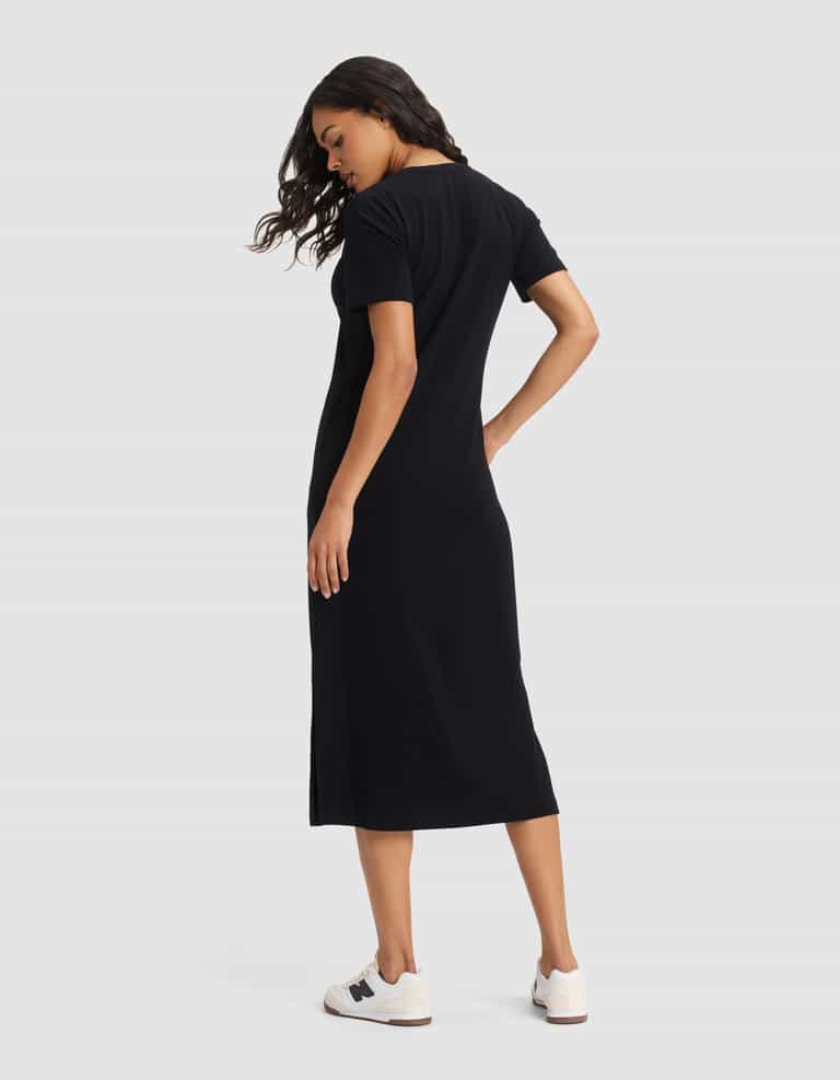 A woman faces away, head turned left, modeling the Cozy Earth Women's Brushed Bamboo Midi Dress in black with short sleeves and white sneakers, set against a plain light background.|Color:Black