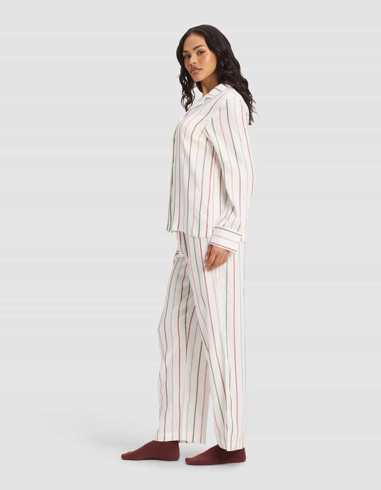 A woman stands sideways wearing the Cozy Earth Women's Soft Woven Long Sleeve Pajama Set with vertical red and gray stripes, paired with dark red socks, against a plain light gray background.|Color:Cottage Stripe