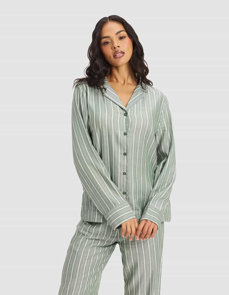 A woman with long dark hair wears the Cozy Earth Women's Soft Woven Long Sleeve Pajama Set in light green with white vertical stripes, standing against a plain light background.|Color:Striped Jasper