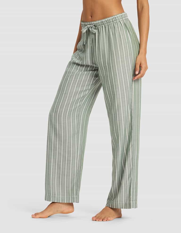 A person is wearing Cozy Earth Women's Soft Woven Pajama Pant in light green with white vertical stripes and a drawstring waist, standing barefoot against a plain light background.|Color:Striped Jasper