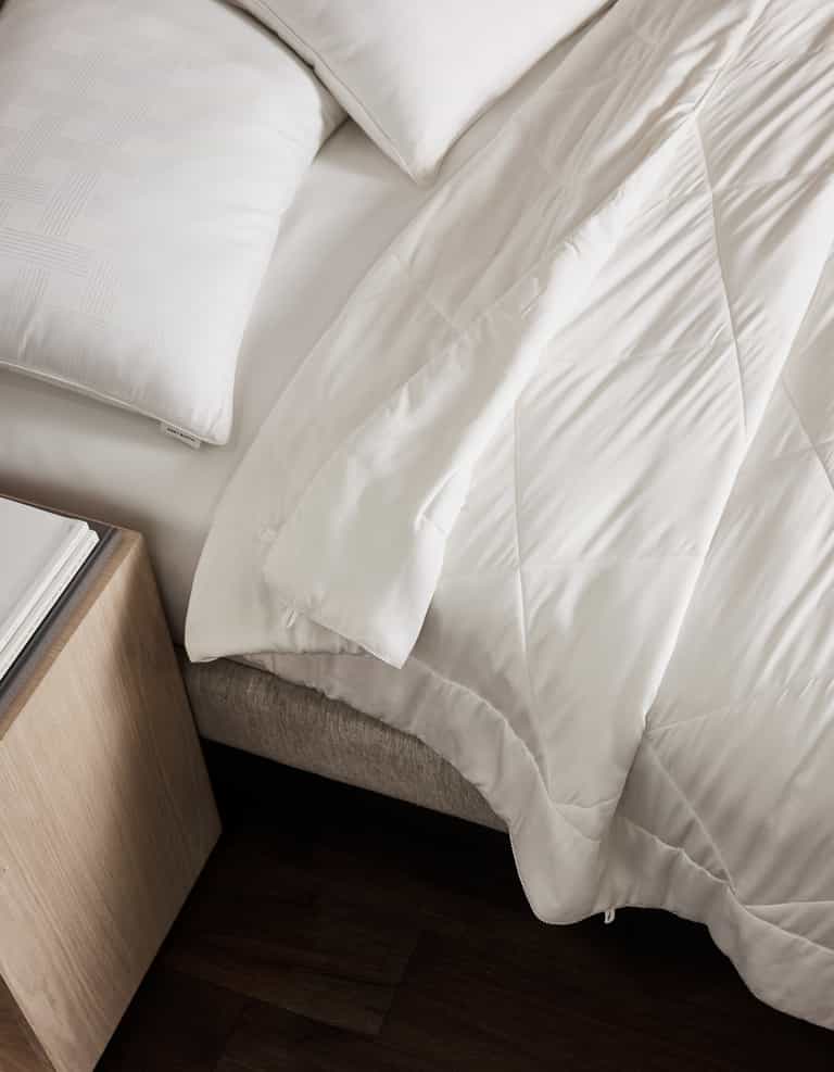 A neatly made bed features white pillows and the Cozy Earth Bamboo Viscose Comforter, partially folded back. Beside it, a light wood nightstand with a book rests on dark wood floors.|Filling:Extra