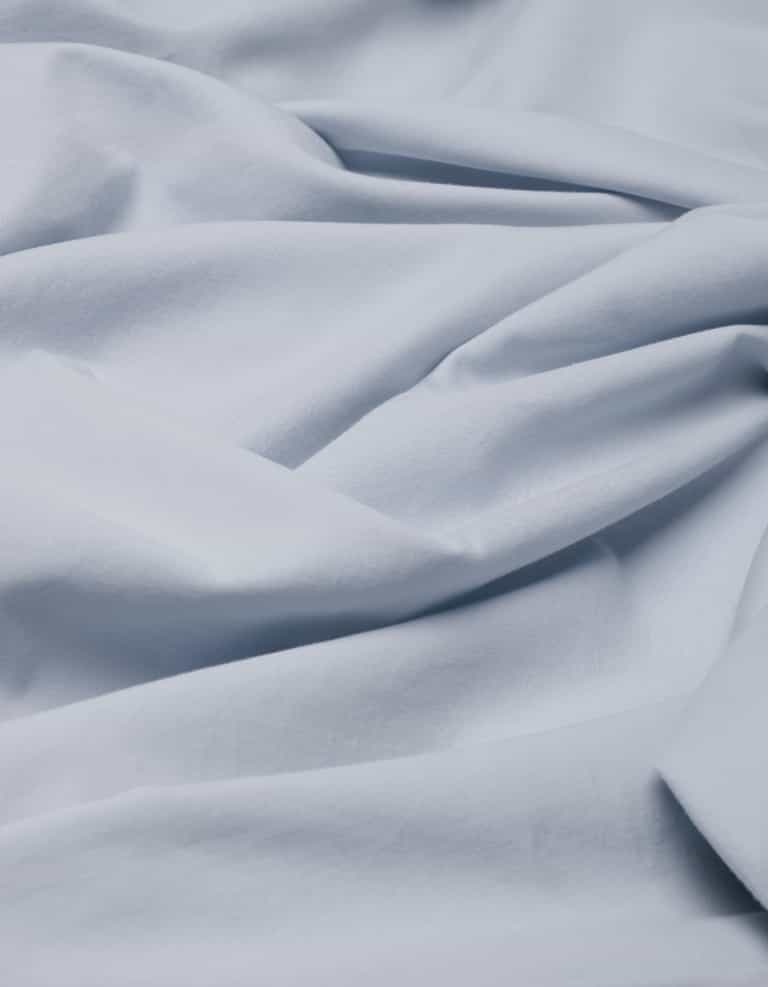 The Cozy Earth Soft-Wash Cotton Flat Sheet features a soft, light blue fabric with gentle folds and creases for a smooth, flowing texture.|Color:Shore