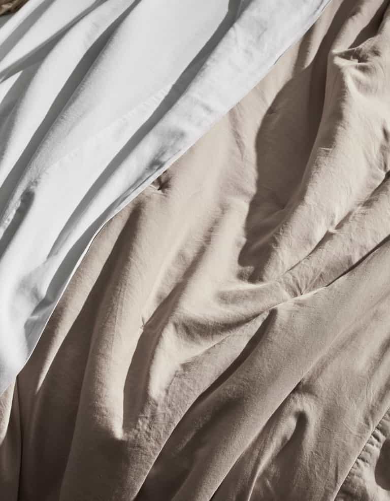 A close-up of the Cozy Earth Soft-Wash Cotton Quilt, showcasing its white and beige tones with gentle, natural light highlighting the soft texture and elegant folds.|Color:Driftwood