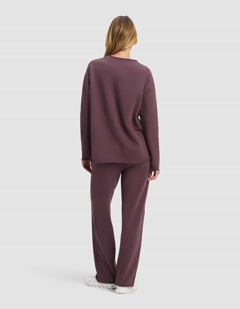 A woman with long hair, seen from behind, wears the Cozy Earth Women's Chelsea Set—a loose-fitting, long-sleeve top and matching pants in muted purple—paired with white shoes against a plain white background.|Color:Fig