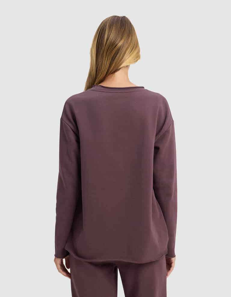 A person with long, light brown hair faces away, wearing the Cozy Earth Women's Chelsea Pullover and matching pants in mauve against a plain light gray background.|Color:Fig