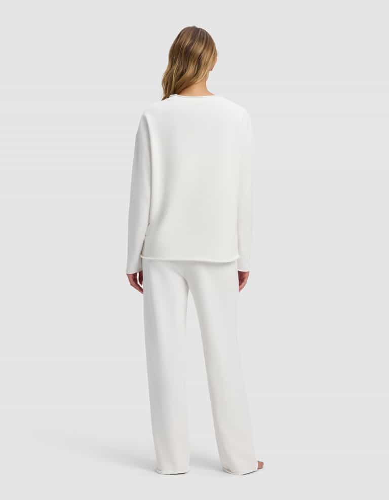 A woman stands barefoot facing away in the Cozy Earth Women's Chelsea Set—loose-fitting white long-sleeve top and pants—against a plain light gray background.|Color:Bone